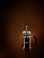 close up view of  french-press filled with fresh black coffee   on brown background