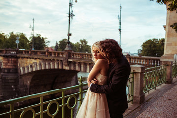 Romantic newlywed couple hugging near bridge over river in Pragu