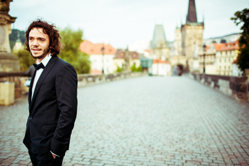 Handsome bearded stylish groom in suit posing on bridge in Pragu