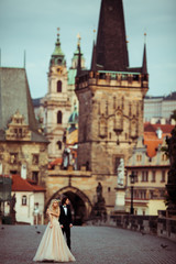 Naklejka na ściany i meble Beautiful blonde bride & handsome groom posing on Prague bridge,