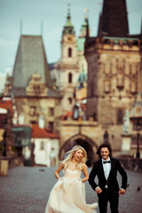 Fototapeta premium Happy handsome groom chasing after beautiful bride on Prague bri