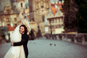 Romantic strong newlywed groom carrying happy bride on bridge in