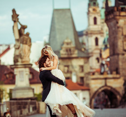 Naklejka premium Romantic strong newlywed groom carrying happy bride on bridge in