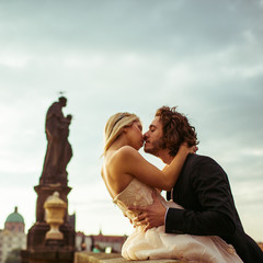 Romantic newlyweds kissing on bridge in Prague, looking at river