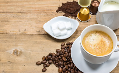 Coffee concept on wooden background.
Cup of creamy coffee, coffee beans, milk, capsules and  sugar.

