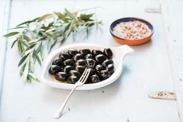 Black olives in white ceramic plate, branches and spices over li
