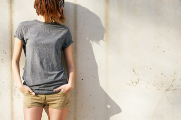 attractive young woman dressed in a gray blank t-shirt posing against a background of a concrete...