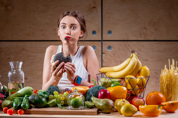 Hungry woman eating black burger at the table full of fruits and vegetables on the wooden...