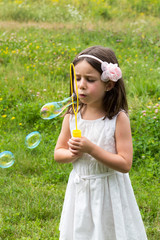 Little girl in white dress blowing bubbles at the park