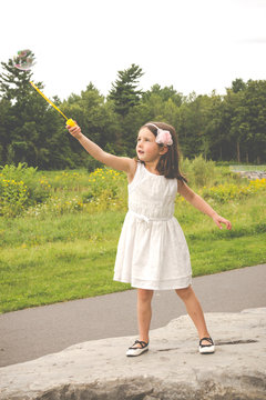Little girl in white dress playing with bubble maker in the park