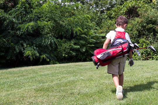 Little boy golfer walking with his golf bag on the fairway