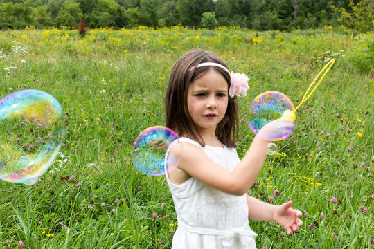 Little girl in white dress playing with bubble maker in the park