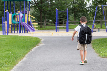 Child with school backpack and book walking in the park