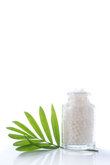 Glass of  homeopathy globules and green leaf