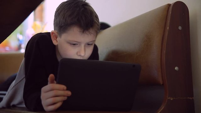 Teen  boy with tablet lying on couch browsing Internet lifestyle
