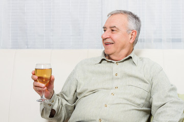 Senior man enjoys drinking wine at home.