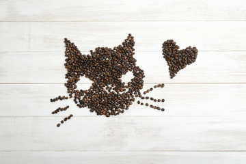 Heart and cat from coffee beans on wooden surface in top view.