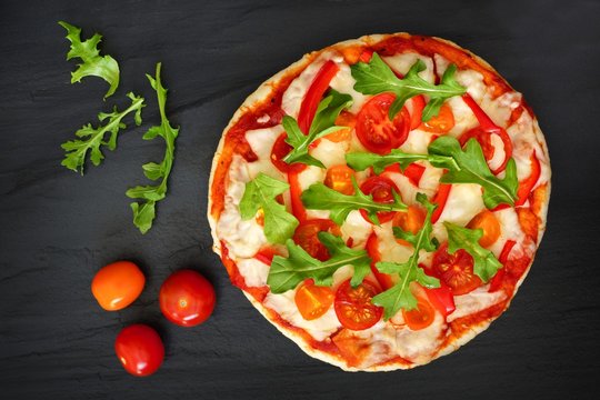 Delicious pizza with arugula and cherry tomatoes against a slate stone background