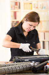 Fototapeta na wymiar Young woman wearing black shirt performing toner change and printer maintenance, concentrated facial expressions