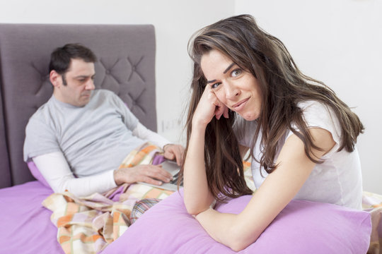 Angry woman sitting in bed, couple is fighting because he's working too much