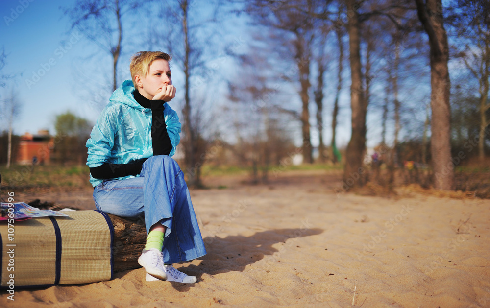 Wall mural blonde in blue windbreaker sitting on log