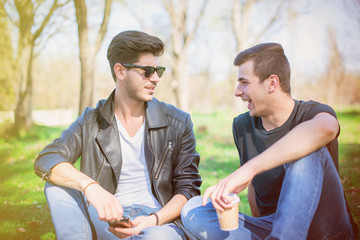 Smiling friends with smartphones sitting on grass in park