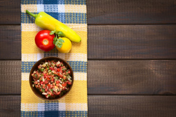 Traditional Chilean Pebre sauce made of tomato, onion, aji verde (small green hot pepper), lemon juice and coriander leaves, photographed on wood with natural light