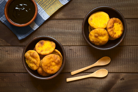 Traditional Chilean Sopaipilla fried pastry made with mashed pumpkin in the dough, served with Chancaca sweet sauce, photographed on dark wood with natural light