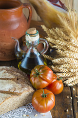 Bodegón de comida con aceite de oliva, pan, tomates, jamón y espigas de cereales en ambiente rústico