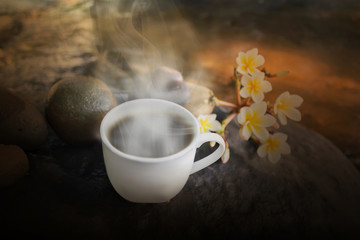 White cup of hot black coffee on waterfall rock with flower 
