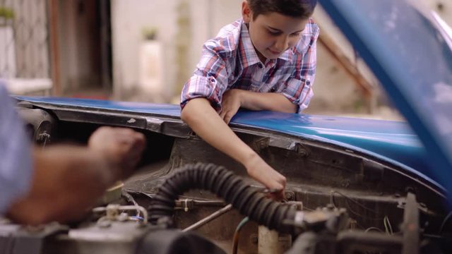 Family and generation gap. Old people spending time with children. The senior man teaches to the preteen child to fix the engine of a vintage car from the 50s. They both smile happy