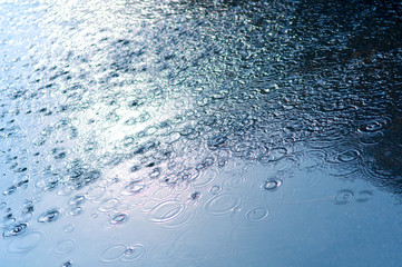 Rain drops background with blue sky reflection and water circles on dark asphalt, on the road
