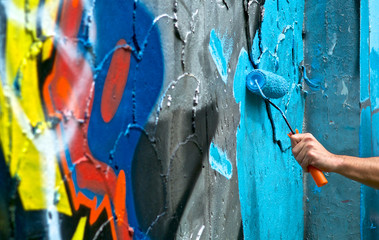 Hand paint roller on a graffiti wall. Peeling spray paint, grunge and texture scratched old cement wall. Close up. © component