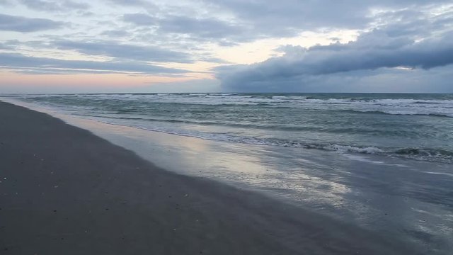 A pale sunrise lights the sky over a beach on the Atlantic Ocean as waves break on the wet sand.