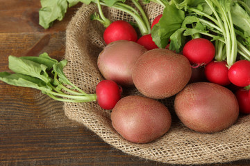 red potatoes on burlap with radishes on wooden brown background