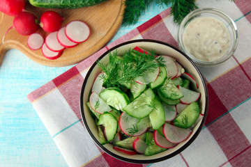 a salad of radish and cucumbers with herbs and salt with sunflower in a bowl near the cutting Board on fabric on wooden background