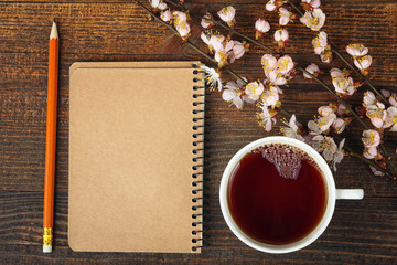 white Cup of tea and a sprig of peach near the Notepad with pencil on a brown wooden background
