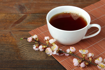 white Cup with tea and a sprig of peach on a brown wooden background