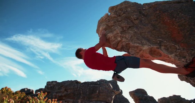 Bouldering rock climber hanging beneath extreme overhang against blue sky