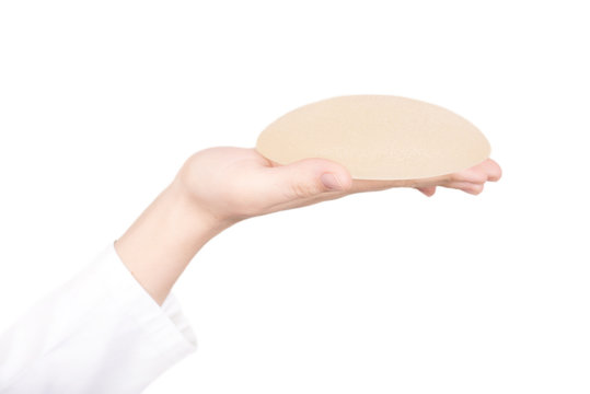 Close up of hand holding silicon breast implant isolated on white background. Plastic surgery concept