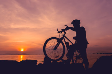 Healthy lifestyle. Silhouette of bicyclist standing with bike at seaside.