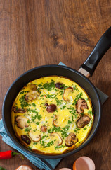 omelet with mushrooms in a frying pan on wooden table