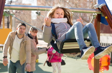 Parents watching little daughters swinging.