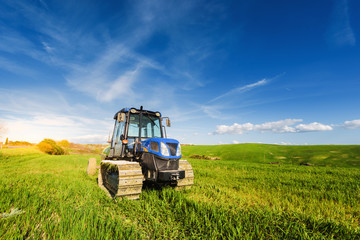 Tractor on tracks in the summer sunny day on a green field.