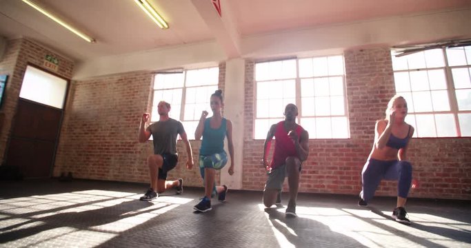 Friends doing jumping lunges during a crossfit workout in the gym