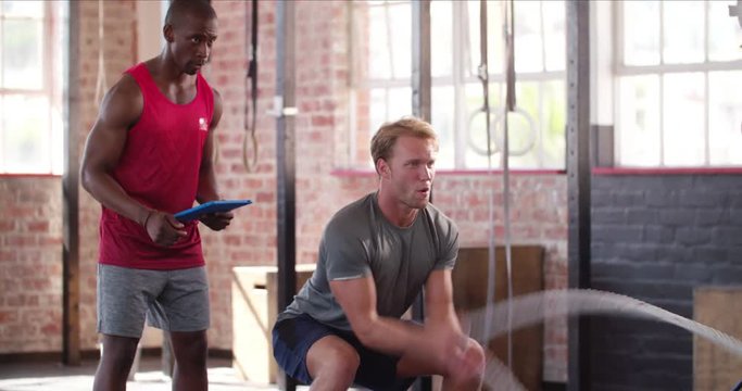 Man learning ropes crossfit workout with a personal trainer with tablet