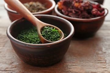 Variety of tea in round bowls with spoon on wooden table, close up