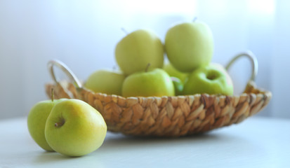 Ripe green apples in a wicker basket on a kitchen table
