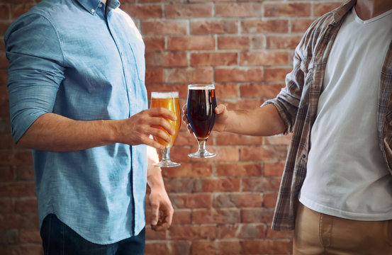 Two men clinking glasses of dark and light beer on brick wall background