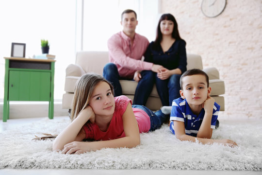 Family portrait of children lying on fur carpet and parents sitting on sofa indoors
